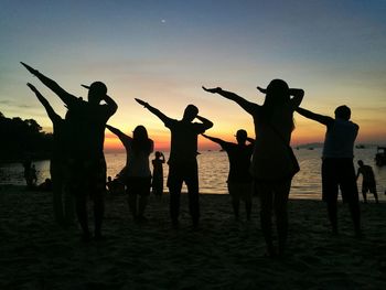 Silhouette people dabbing on beach against sky during sunset