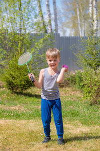 A fair-haired child plays badbinton on the lawn