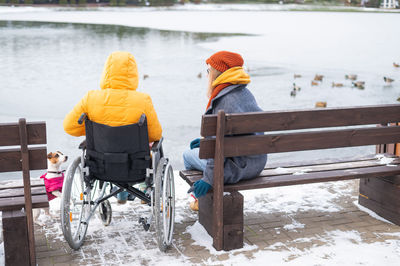 Caucasian woman in a wheelchair and her friend are sitting by the lake with ducks in winter