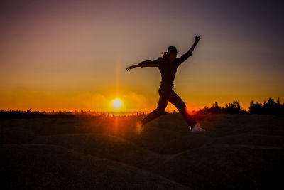 Rear view of woman jumping against sky during sunset
