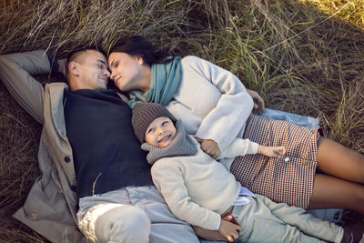 Family of three with a boy child mom and dad are lying on a field in autumn at sunset
