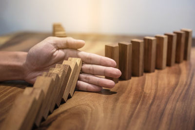 Cropped hand of man blocking wooden dominoes on table