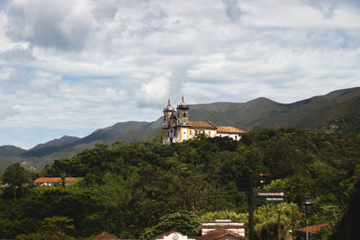 Built structure by trees and mountains against sky