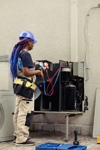 Full length of woman using mobile phone while standing against wall