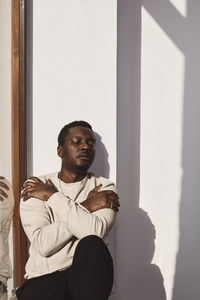 Mid adult man hugging himself against white wall