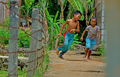 Full length of shirtless boy with sister by fence