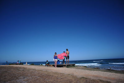 People on beach against clear blue sky