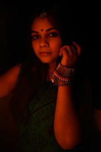 Portrait of young woman wearing jewelry and bindi in darkroom