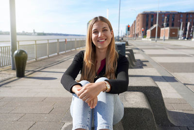 Young beautiful woman sitting relaxed on liverpool waterfront on sunny day, england