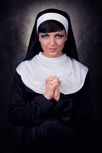 Portrait of smiling nun standing against black background