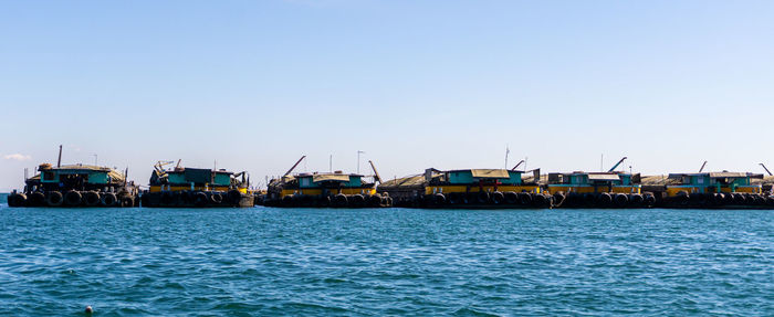 Fishing boats in sea against clear blue sky