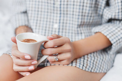 Woman in plaid pajama shirt is sitting in bed with cup with hot coffee. engagement and wedding rings