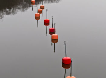 Close-up of red and orange buoys floating on lake against sky