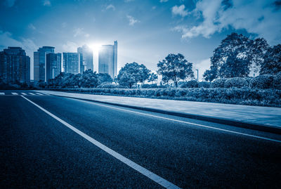 Road by buildings against sky in city