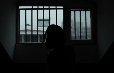 Silhouette woman looking through window