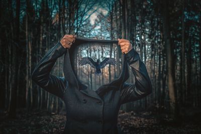 Digital composite image of woman holding hood with pigeon flying in forest