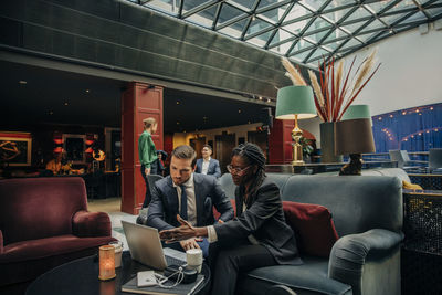 Young businesswoman discussing over laptop with male colleague in hotel lounge