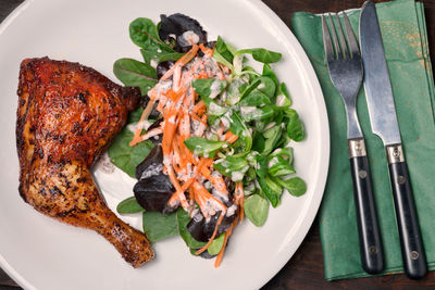 High angle view of grilled chicken leg with mixed salad served on table