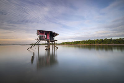 Stilt house on lake against sky