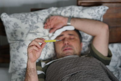 Man checking temperature while lying on bed at home