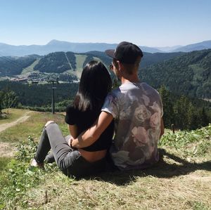 Rear view of couple sitting on mountain against clear sky