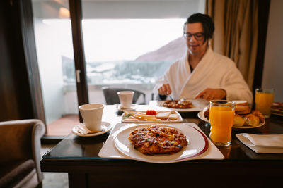 View of man in bathrobe sitting and having breakfast in room