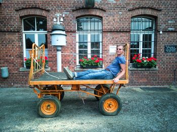 Side view of man sitting on cart by building