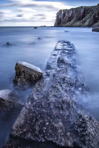 Scenic view of rocks at sea shore against sky