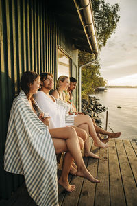 Male and female friends sitting near cottage with legs crossed at knee during sunset