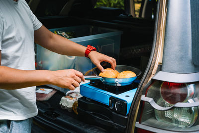 Midsection of man preparing food on camping stove in car trunk