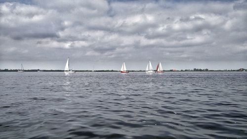 Boats sailing in lake against cloudy sky