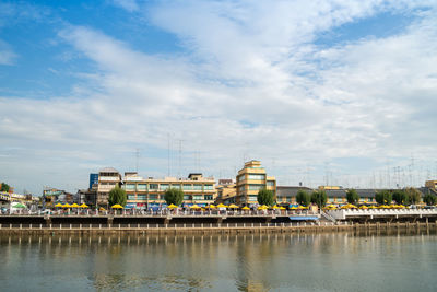 Buildings at waterfront against cloudy sky