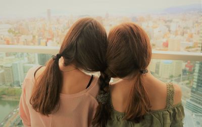 Rear view of sisters with braided hair against window