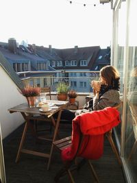 Side view of woman drinking drink while resting on balcony in city