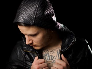 Close-up of young man wearing leather jacket against black background