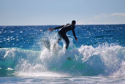 Teenage boy surfing in sea against sky