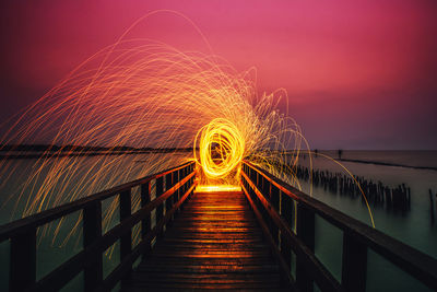 Wire wool spinning on pier over lake against dramatic sky during sunset