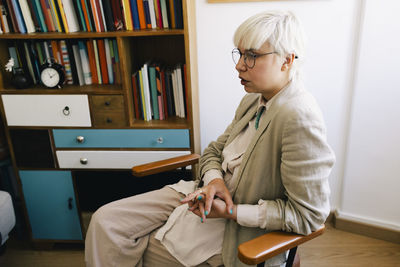 Female therapist sitting with hands clasped on chair in office