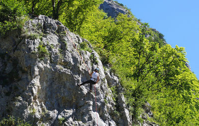 Low angle view of man climbing on rock against sky