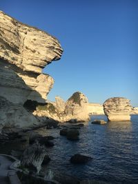 Rock formations in sea against clear blue sky