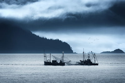 Silhouette fishing boats in sea against cloudy sky