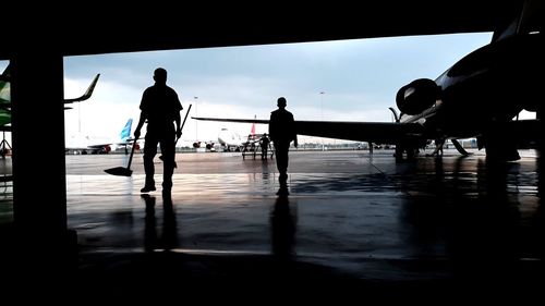 Silhouette people walking on wet airport against sky