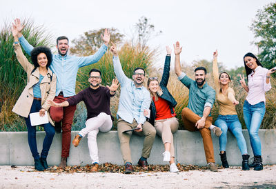 Full length portrait of happy young friends standing against the sky