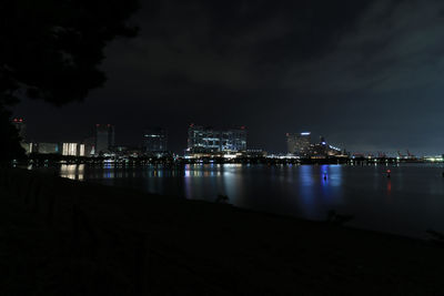 Illuminated buildings by river against sky at night