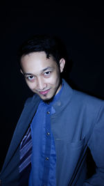 Portrait of young man standing against black background