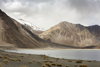 Scenic view of lake by mountains against cloudy sky