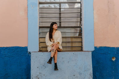 Dark-haired female model in vintage clothing and make-up against a colorful wall.
