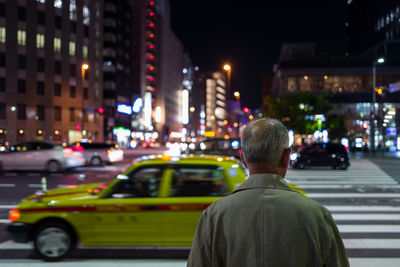 Rear view of man standing on road in city at night