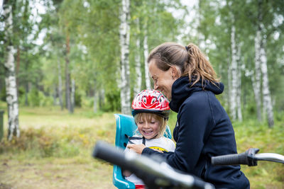 Woman fastening belts for daughter sitting on bike seat