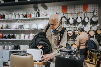 Senior man examining toaster while shopping in appliances store